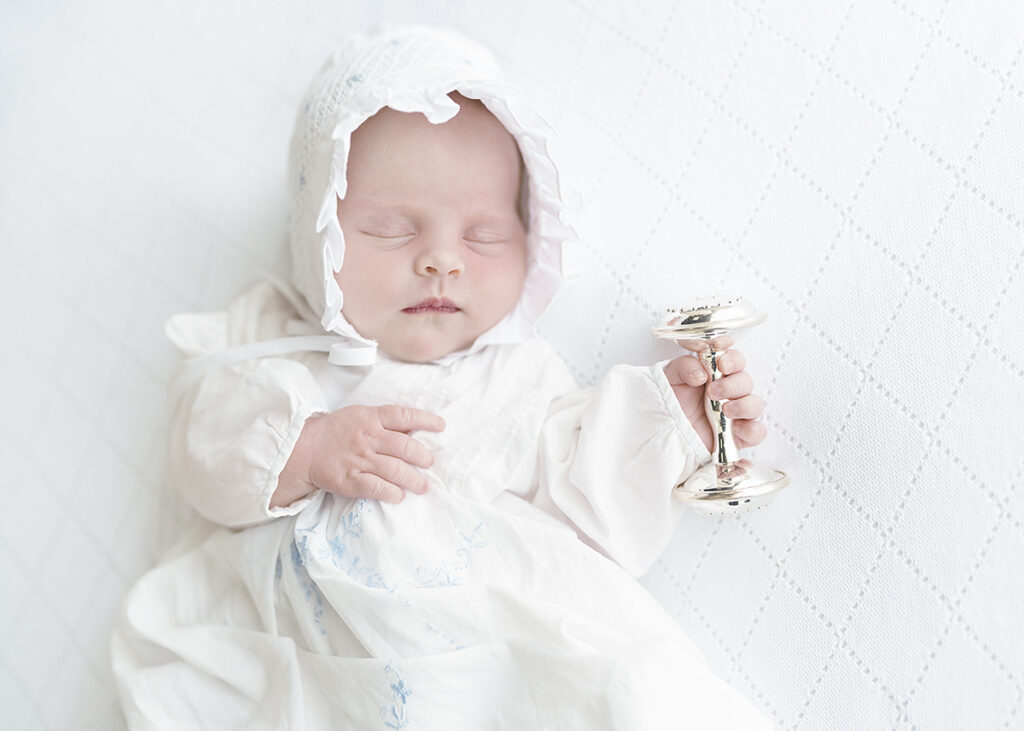 newborn baby girl photographed in a grandmillenial style dress with silver rattle