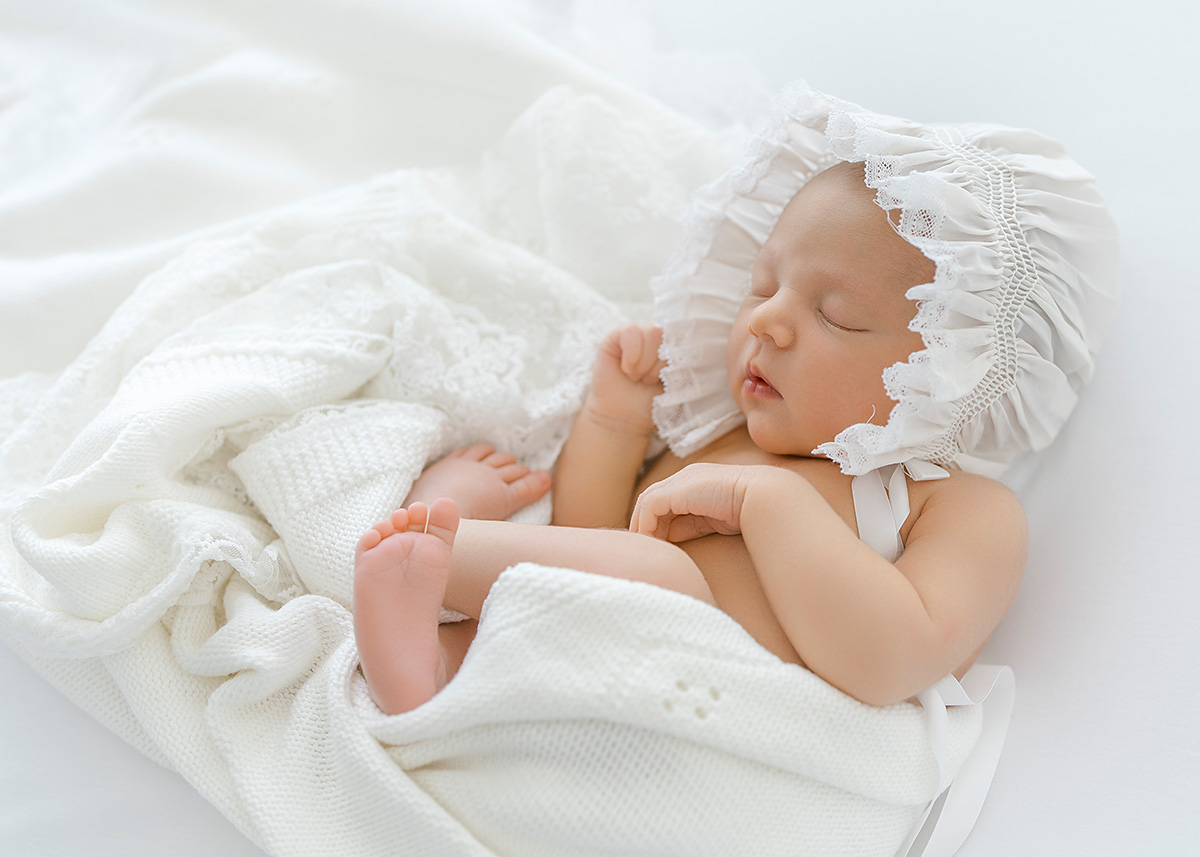 baby girl photographed in a simple and timeless way on a white background wearing feltman brothers bonnet and wrapped in a feltman brothers blanket